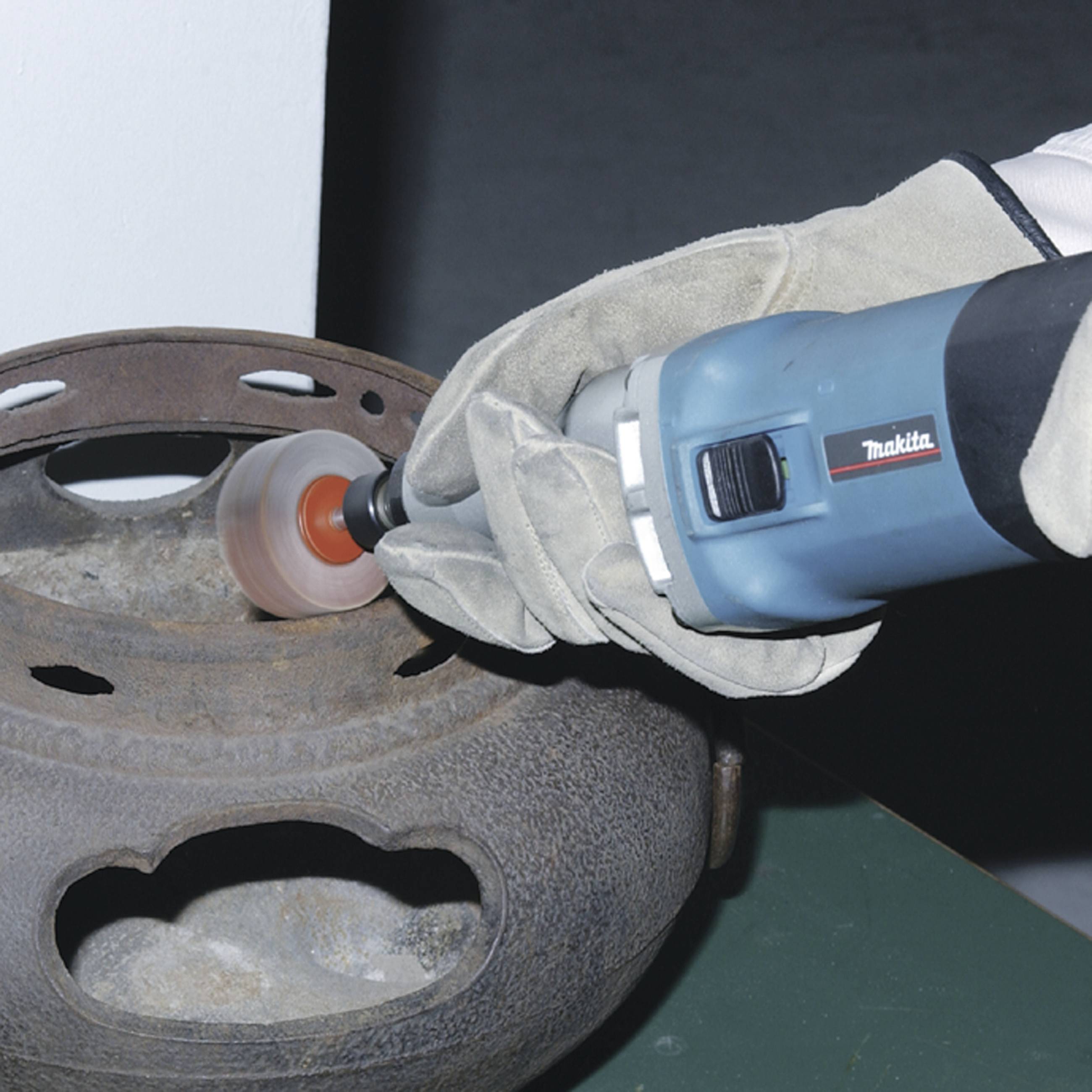 A person is grinding rust off a metal pot with a blue electric tool.