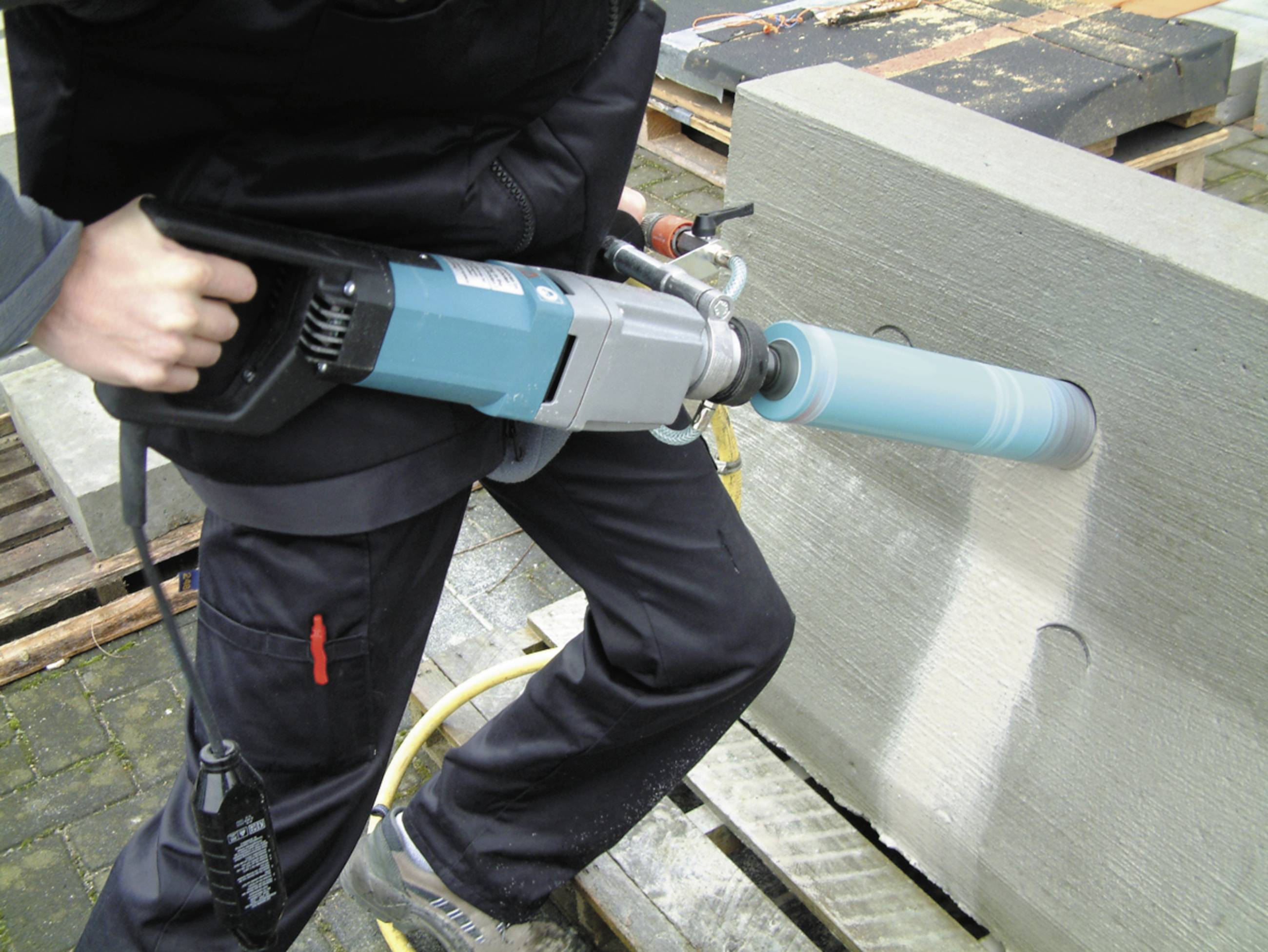 A person is using a hammer drill to bore a circular hole in a concrete block.