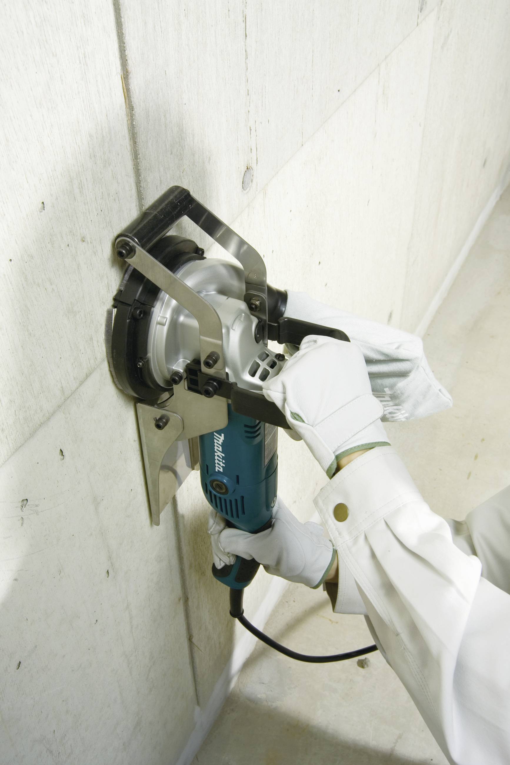 A person wearing white gloves is holding an angle grinder, cutting a concrete wall. Protective measures are visible.