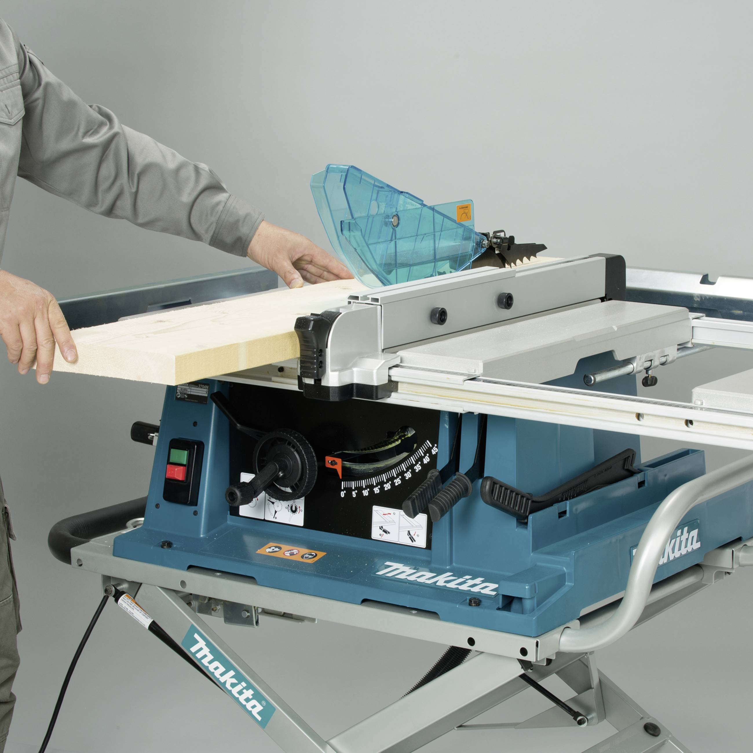 A person is operating a table circular saw and cutting a wooden board. The saw has a blue protective cover and a guide rail.