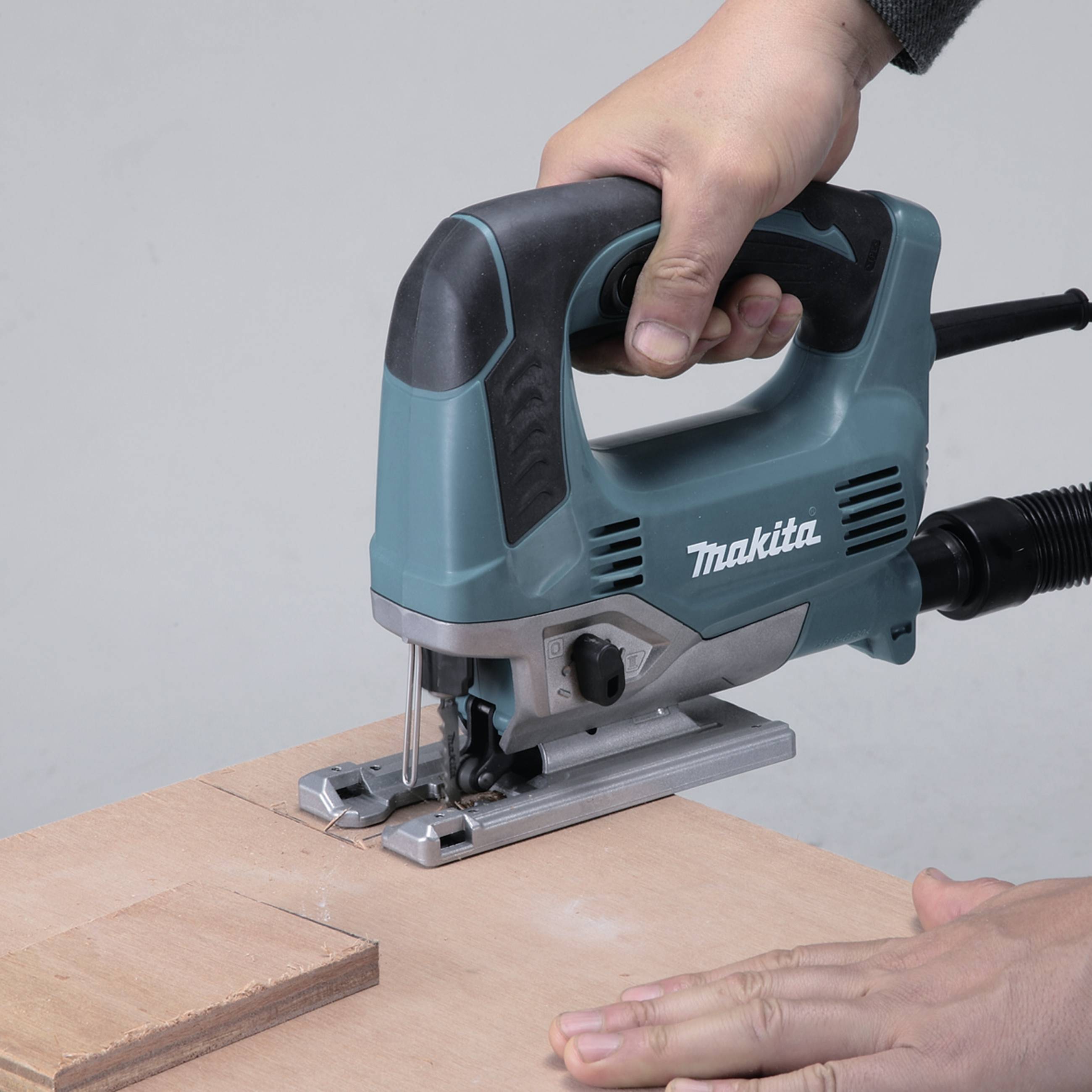 A hand is operating an electric jigsaw, cutting a piece of wood on a table.