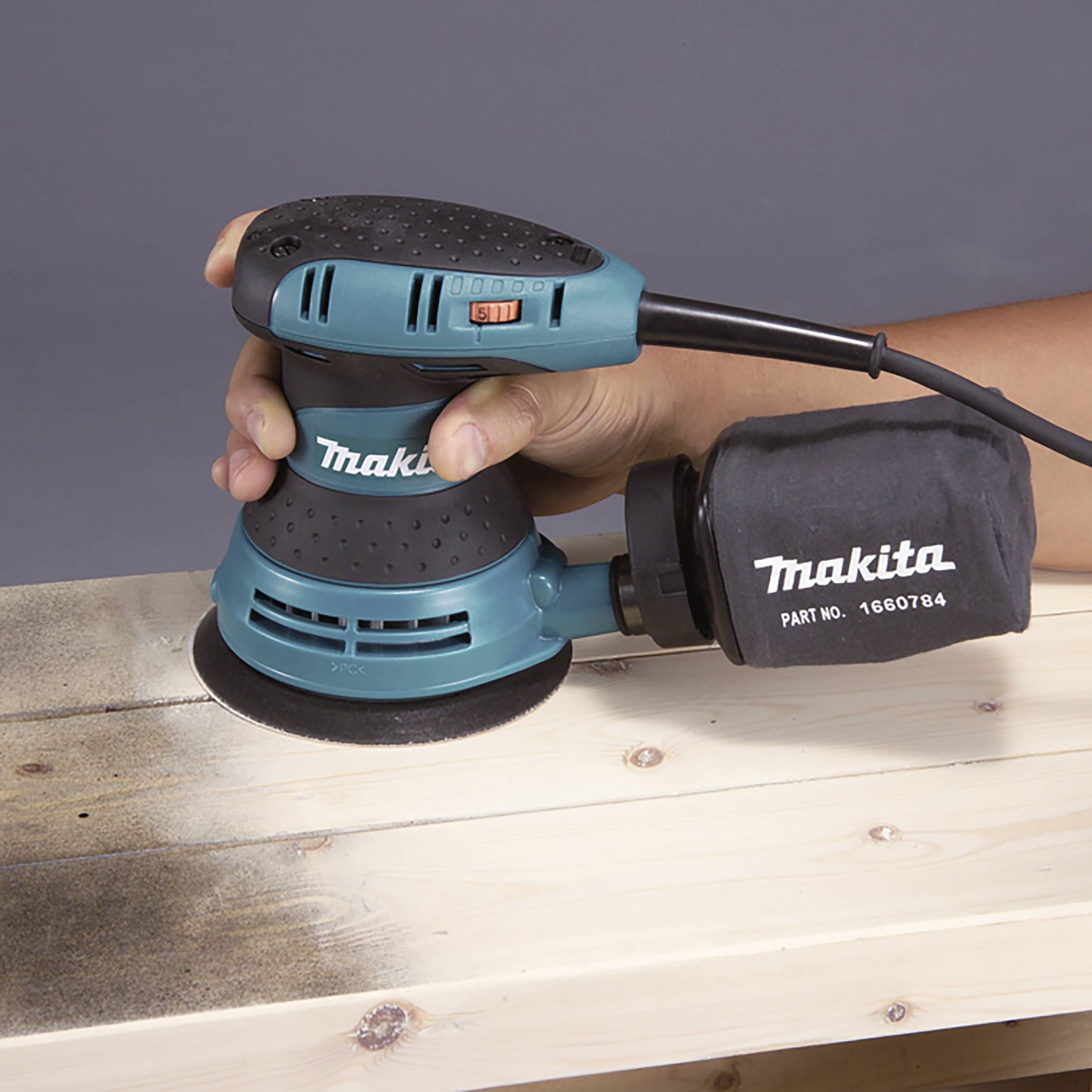 A person is using an electric sanding tool to smooth the surface of a wooden beam. The tool and dust bag are visible.