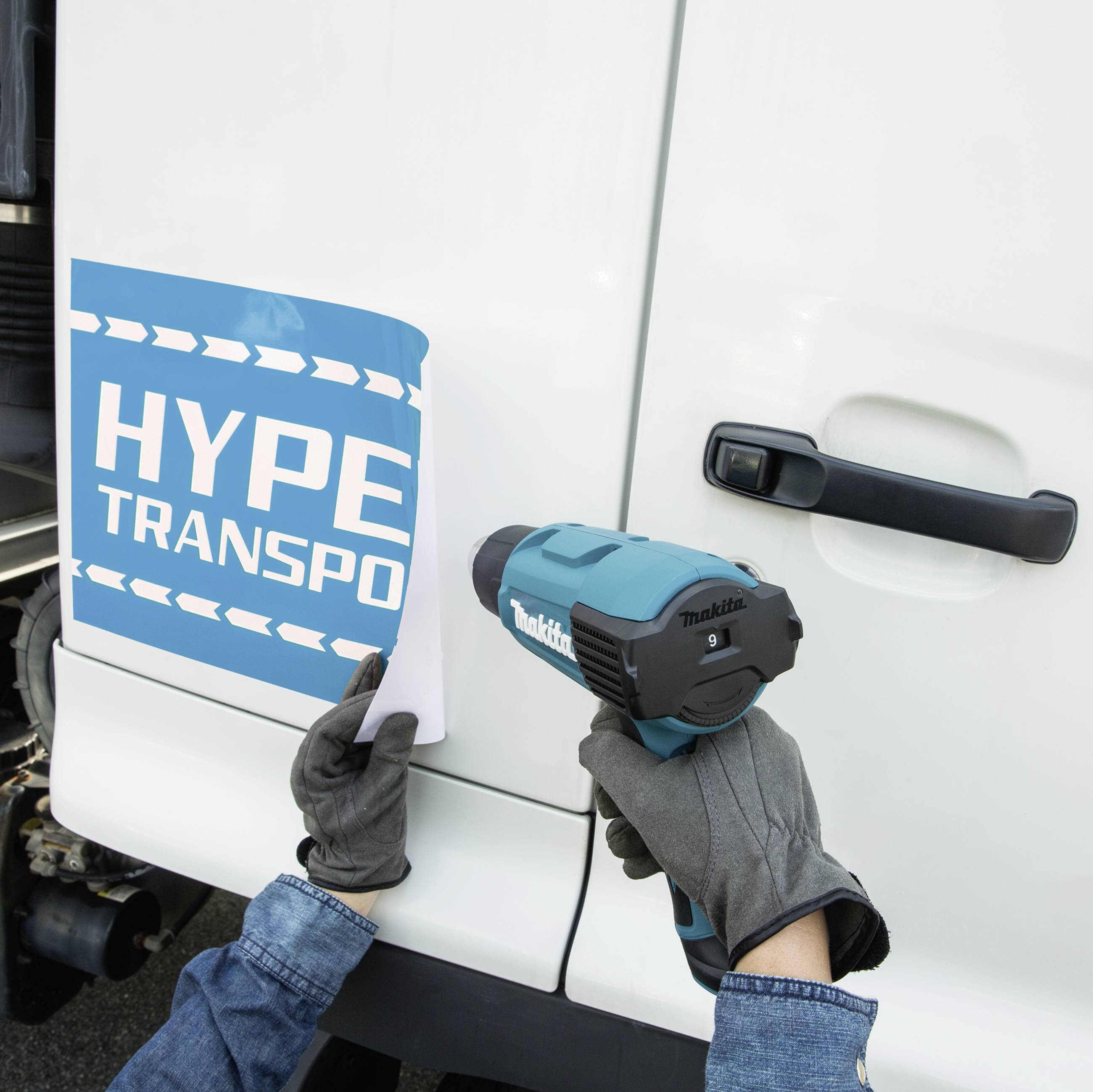 A person is sticking a blue sign with the inscription 'HYPER TRANSPORT' on the side of a vehicle.