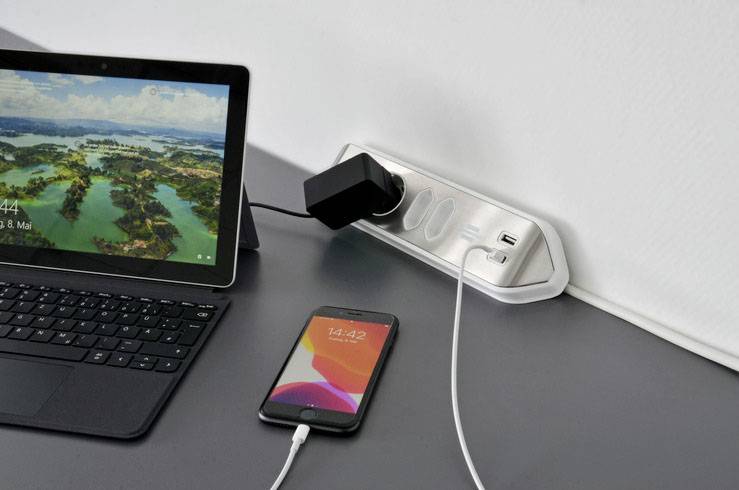 'A tablet displays a landscape with a date, a smartphone is being charged at a multi-socket power strip.'