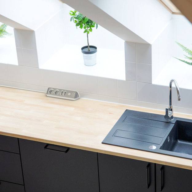 Kitchen with a black sink on a wooden worktop, an angled window above, and a potted plant between the tiled splashback and socket.