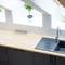 Kitchen with a black sink on a wooden worktop, an angled window above, and a potted plant between the tiled splashback and socket.