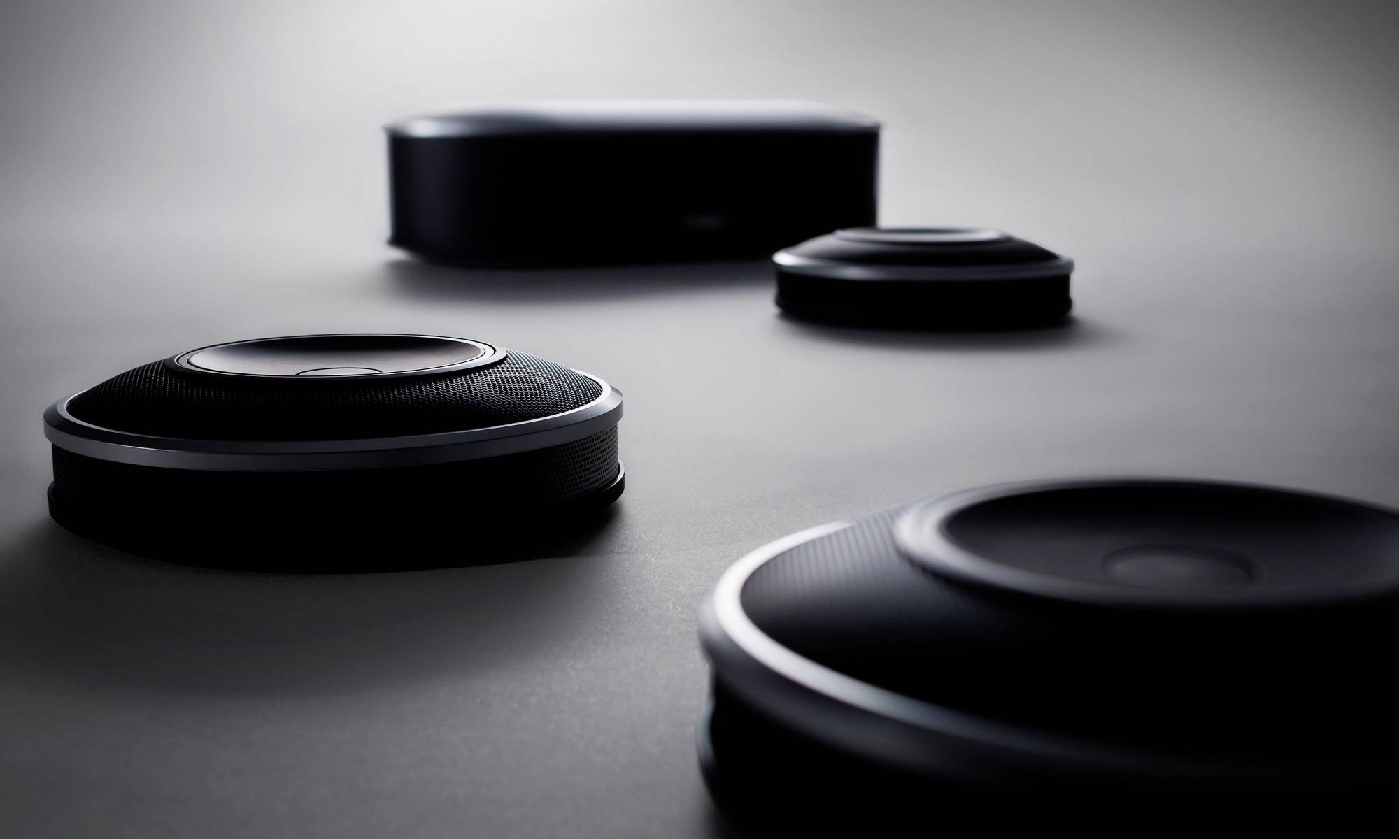 Several black speakers in various sizes on a grey surface, with blurred background.