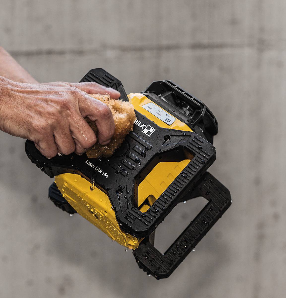 A hand is cleaning a yellow, angular device with water.