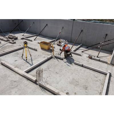 A construction worker in protective clothing is measuring the floor plan of a building on a construction site, surrounded by surveying equipment.