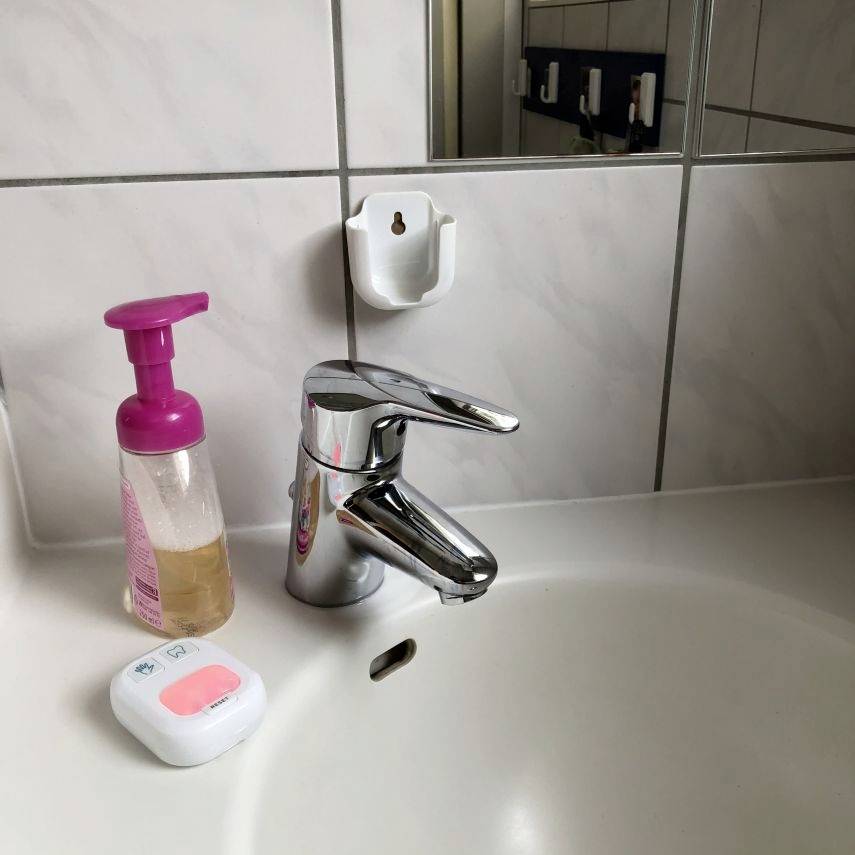 A washbasin with a tap, to the left a liquid soap dispenser bottle with a pink pump and a rectangular soap dish.