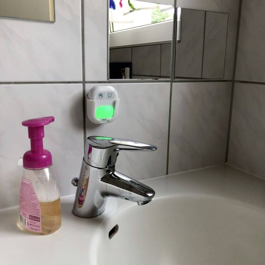 There is a bathroom sink with a tap and a pink soap dispenser on top of it. Mirrors can be seen in the background.