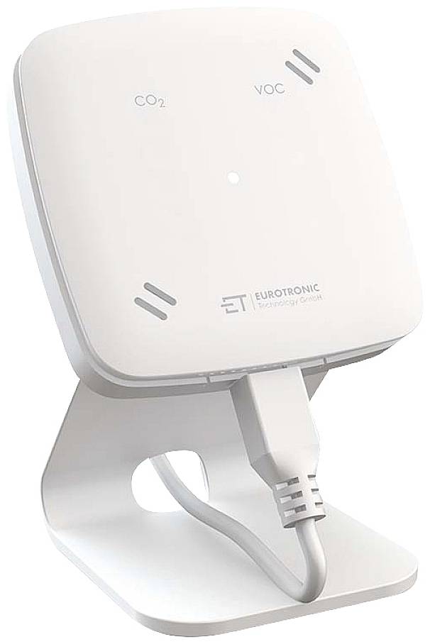 A white indoor air quality monitor measures CO2 and VOC levels in the air, positioned on a stand, with a connected cable.