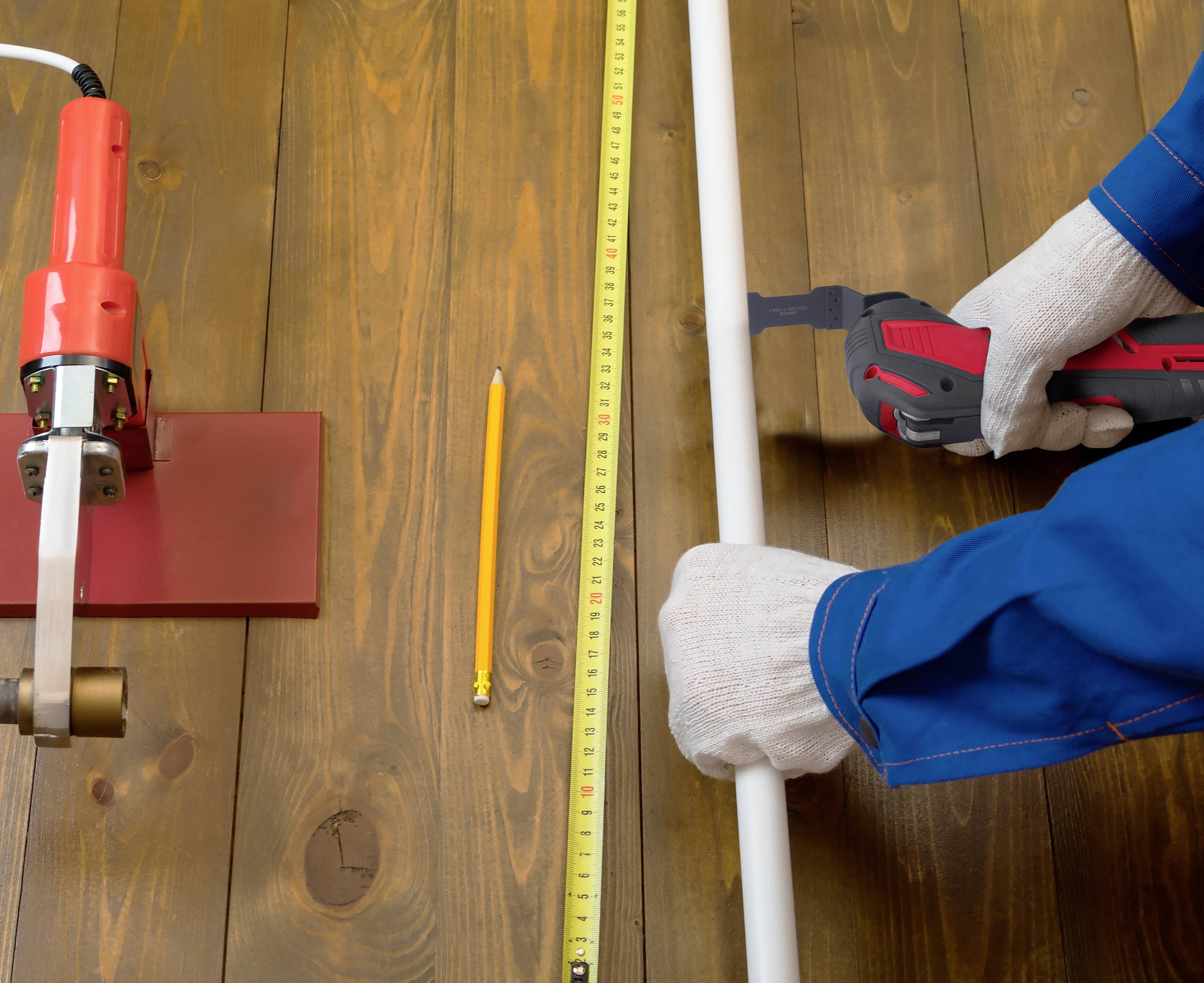 A person in protective clothing is measuring a white pipe with a tape measure on a wooden table.