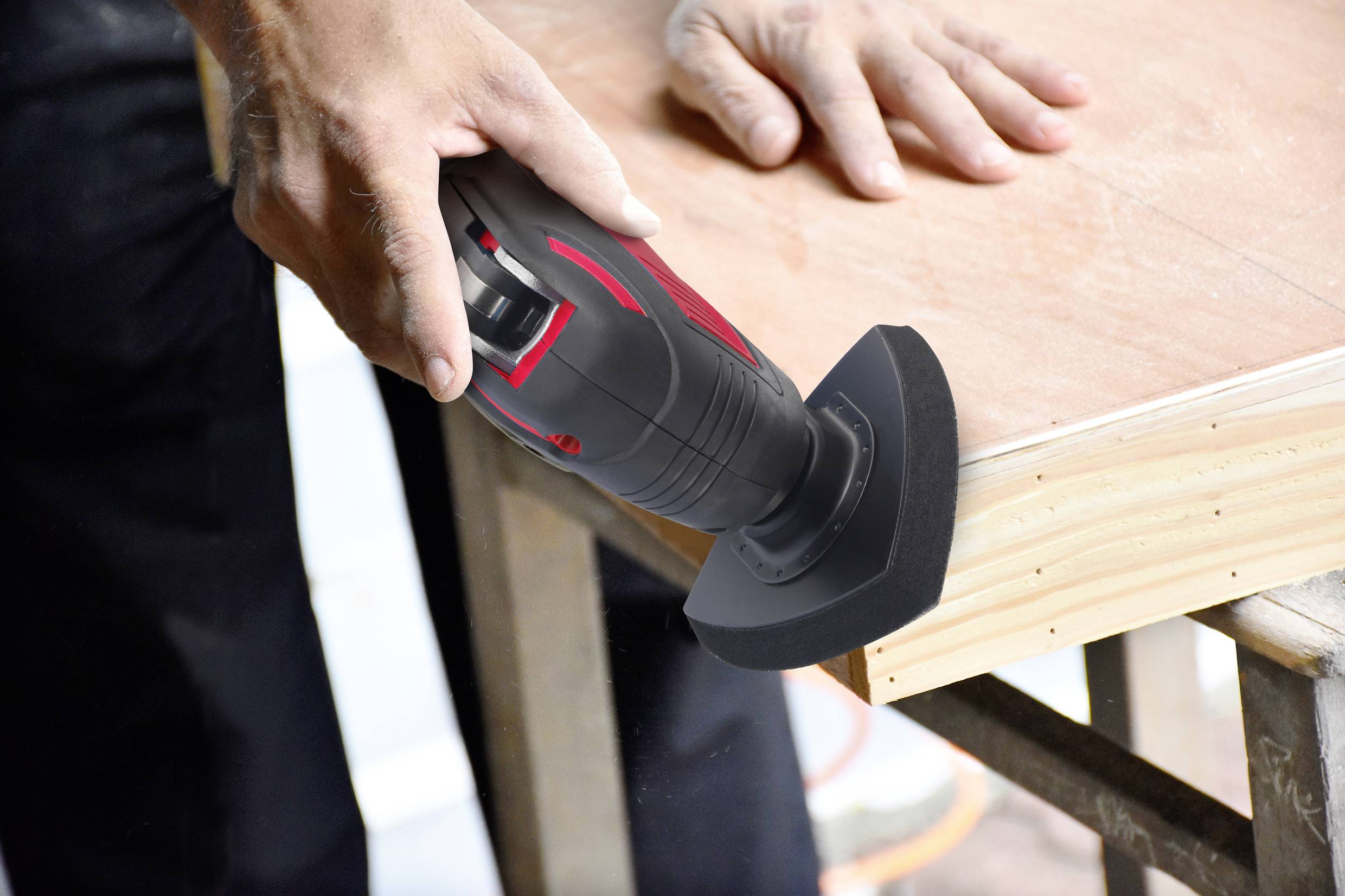 A person is sanding the edge of a wooden board with an electric handheld sander for smooth surface finishing.
