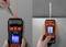 A person is using a laser distance measuring device to measure a distance. A laser is aimed at a wall on the left, and the device shows a measurement reading on the right.