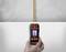 A hand is holding a digital locator device that is detecting a vertically running pipe in the wall.