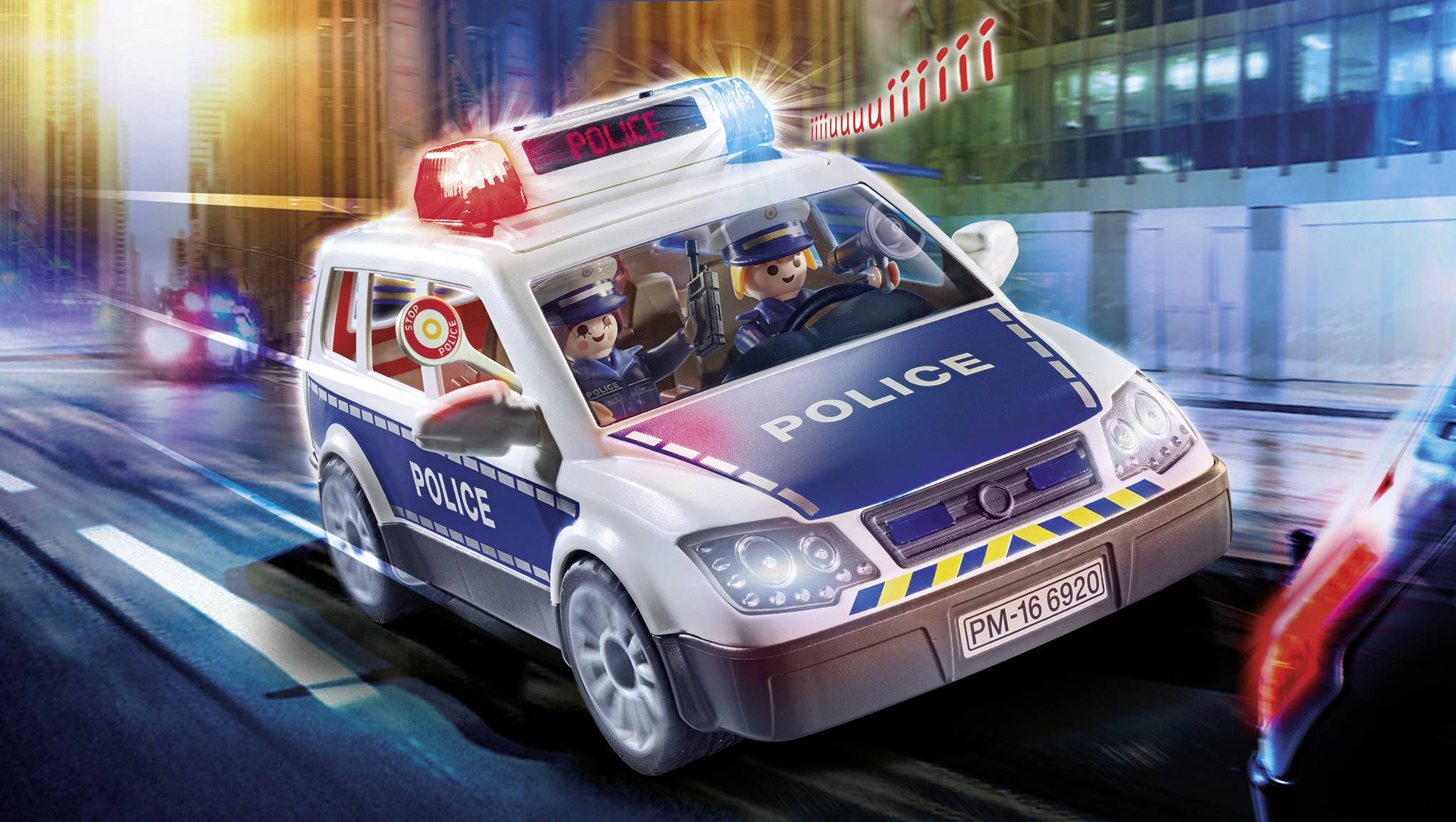 A toy police car with flashing lights speeds through a city. Two toy figures in police uniforms are sitting in the car.