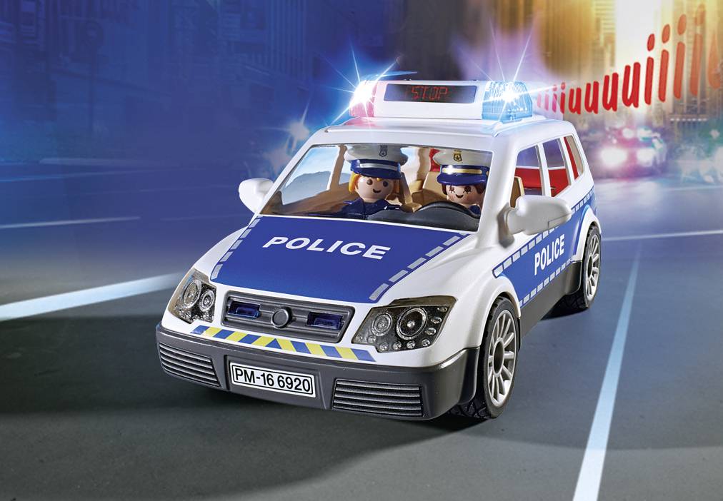 A toy police vehicle with flashing lights drives along a road. Two figures in uniform are seated inside the vehicle.
