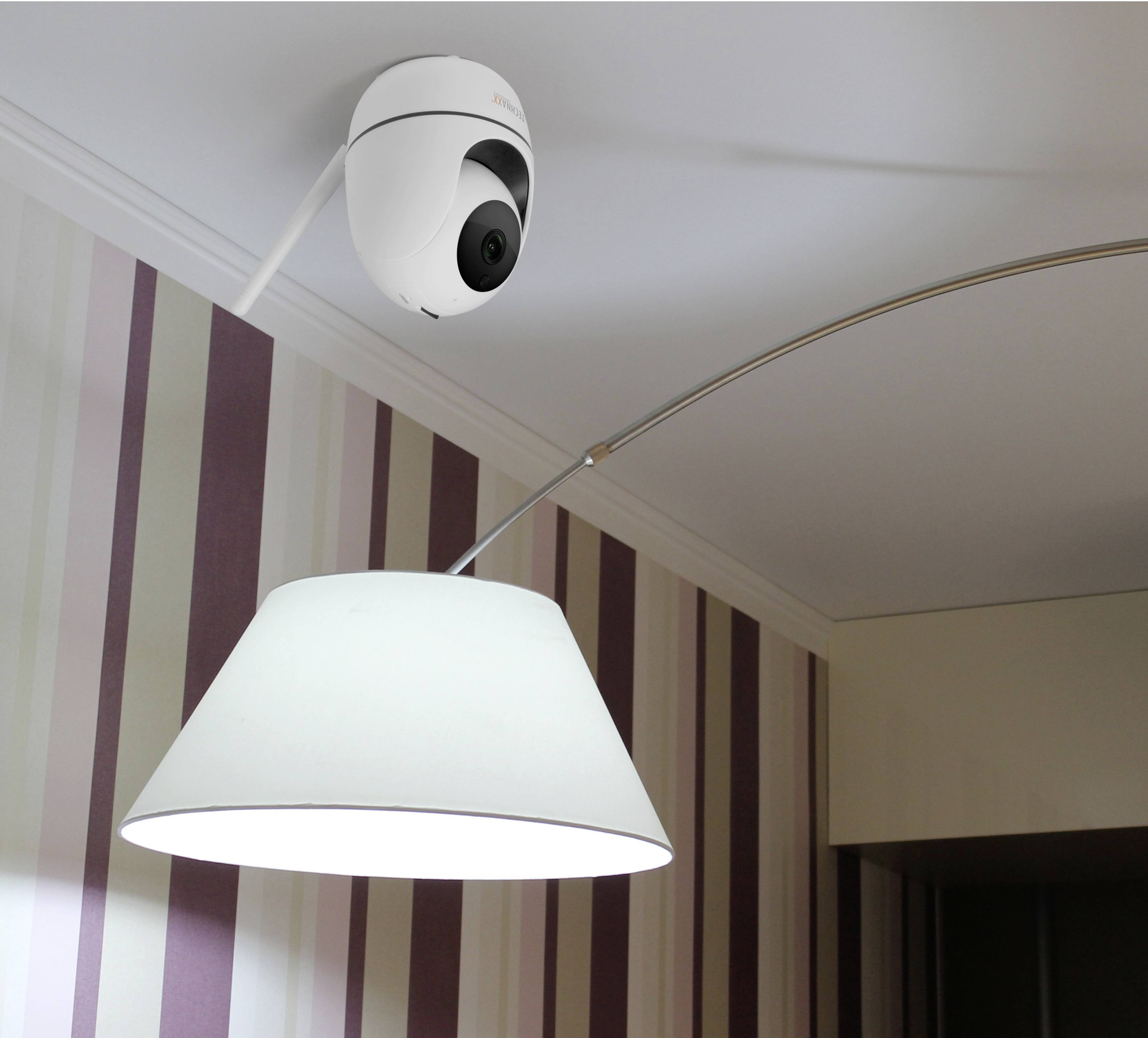 A ceiling-mounted security camera looking into a room with striped wallpaper and a white pendant light.