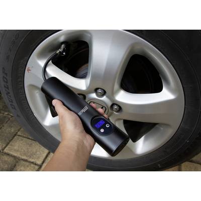 A handheld device measures the tyre pressure of a car tyre. The display shows '2.55'. The tyre is standing on a paved surface.