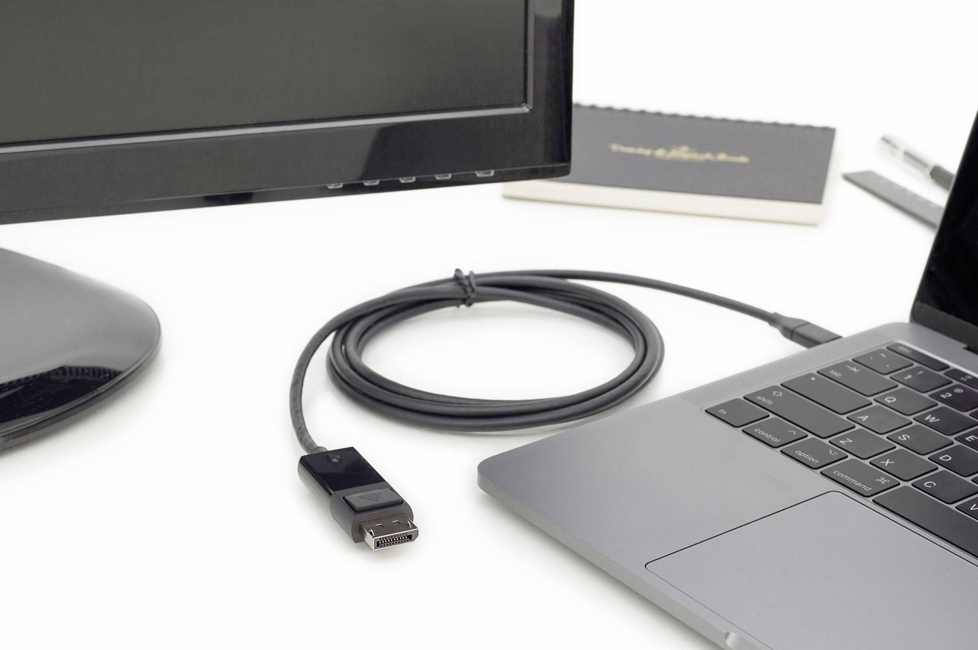 Laptop and monitor connected with a black cable on a desk. A notebook and pen are in the background.