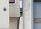 A modern video doorbell with a camera mounted on an exterior wall next to a blue door, with a smart speaker installed inside on the wall.