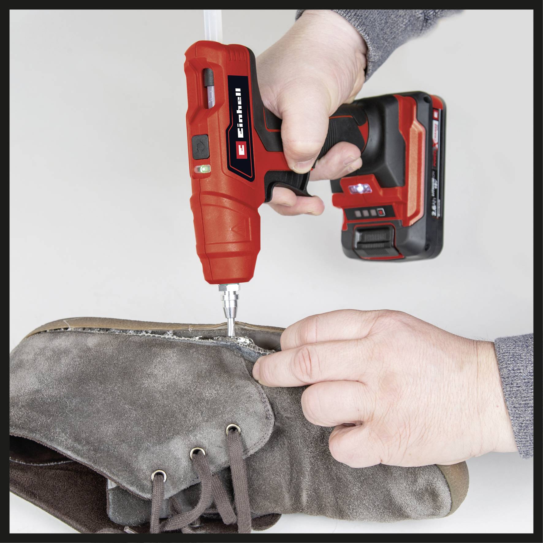 A person is sewing a grey boot edge with a red, cordless handheld tool.