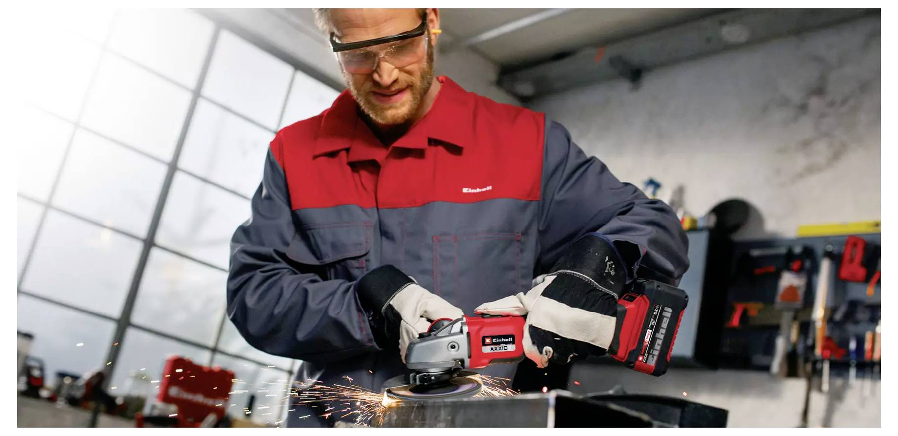 A person wearing safety goggles and gloves uses a power tool to grind metal in a workshop, with sparks flying from the tool.