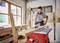 A man is working in a woodwork workshop, sawing a plank with an electric table saw. Surrounded by wood and tools.