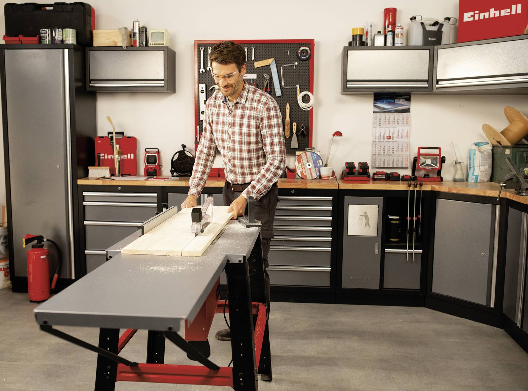 A man is working with a circular table saw in a workshop. Surrounded by tools and shelves, he is cutting wood to size.