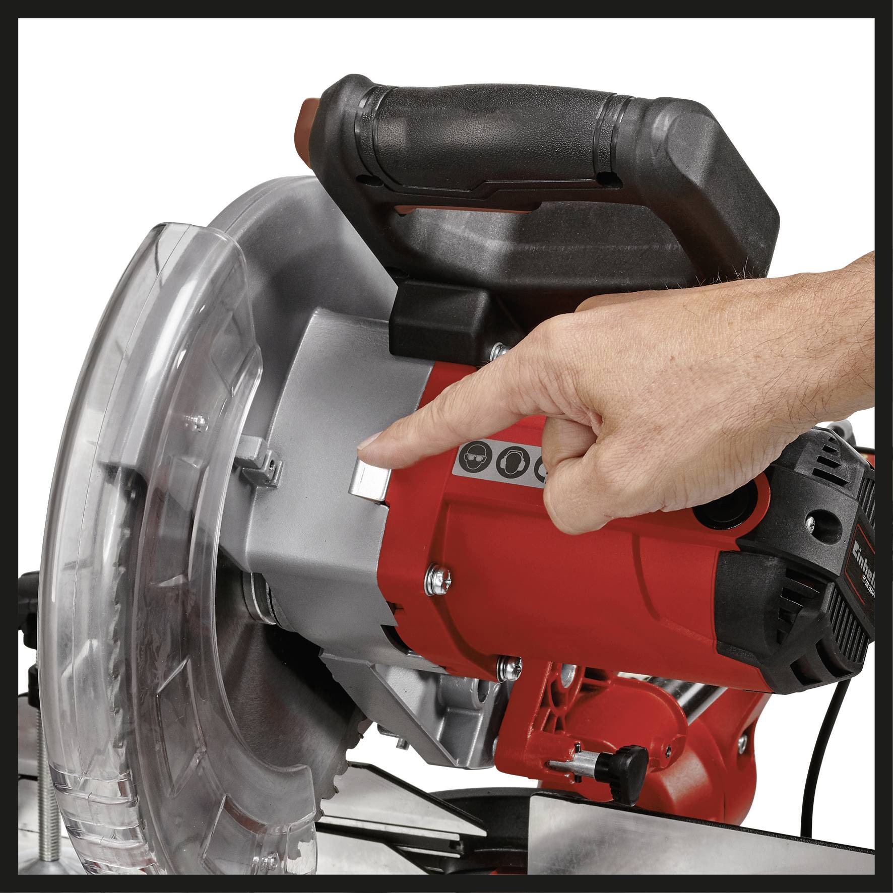 A hand operates the switch of a red electric saw with a safety guard.