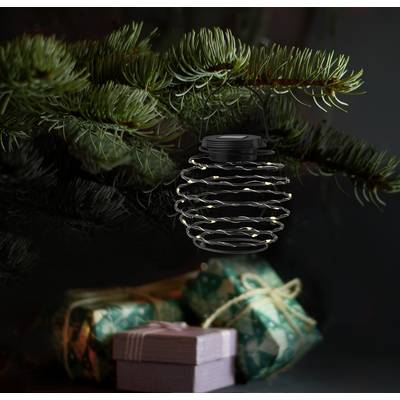Lantern with fairy lights hangs on pine branches, with gifts wrapped in green and pink paper underneath. Festive Christmas decoration.