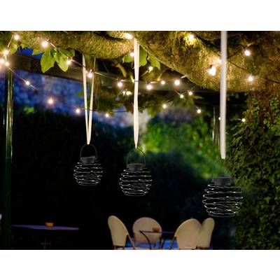 Three hanging lanterns beneath an illuminated tree in the garden. In the background, blurred chairs and a table are visible.
