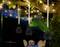 Three hanging lanterns beneath an illuminated tree in the garden. In the background, blurred chairs and a table are visible.