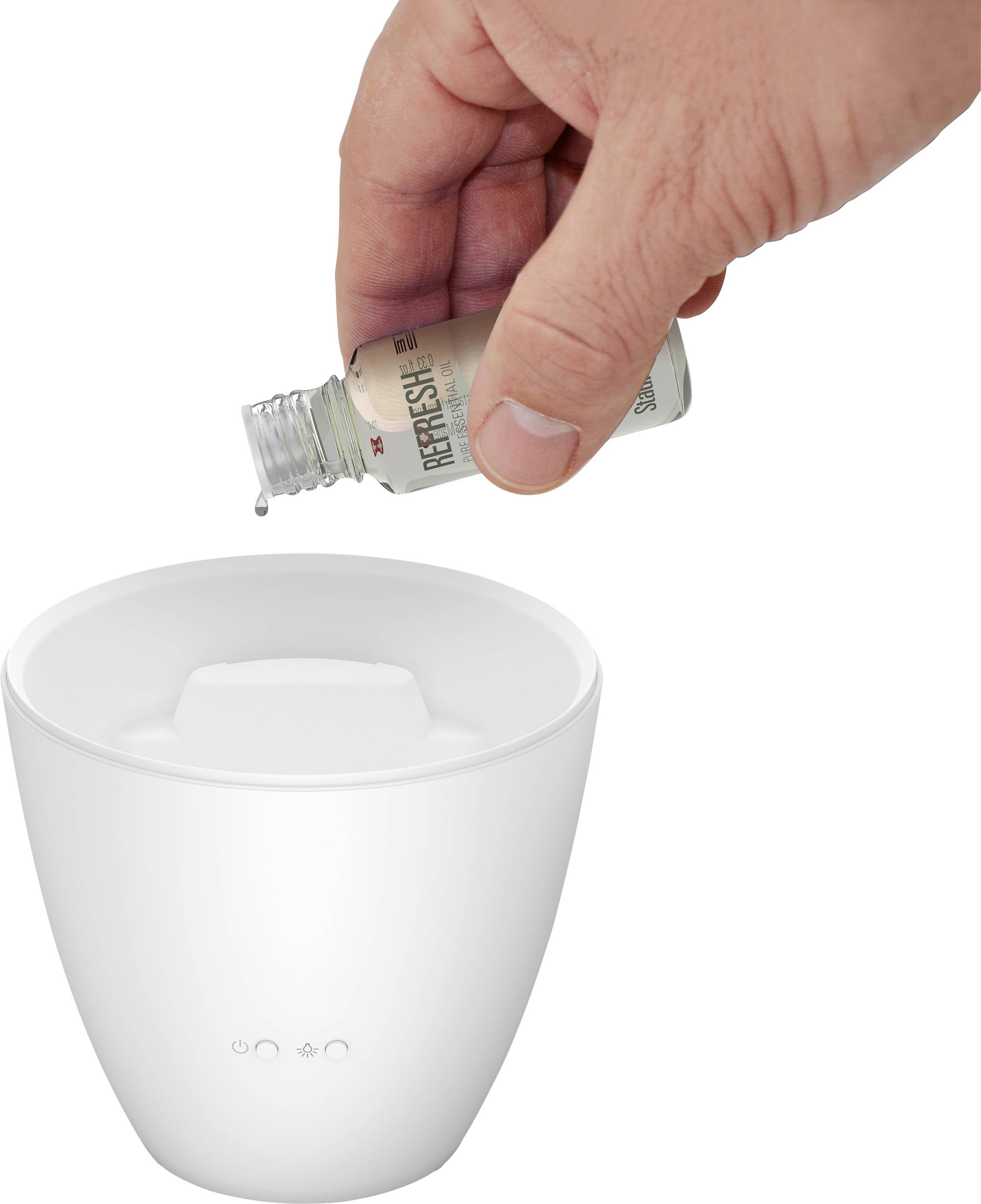 A hand is pouring a small amount of liquid from a small glass bottle into a white humidifier.