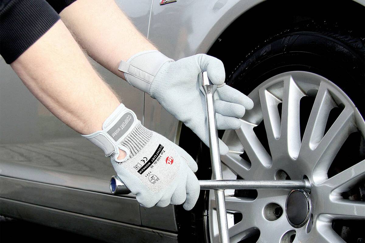 A hand wearing a glove uses a cross wrench to tighten a wheel nut on a car tyre. Safety precautions during tyre changing.