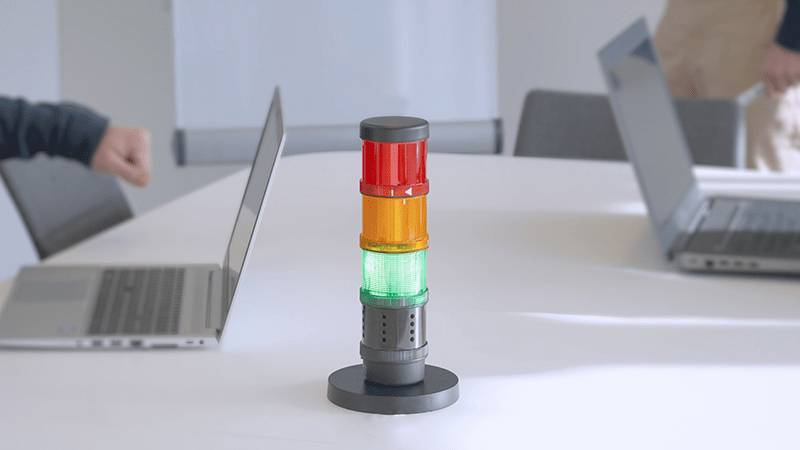 A traffic light with red, yellow, and green lights stands between two laptops on a table in a meeting room.