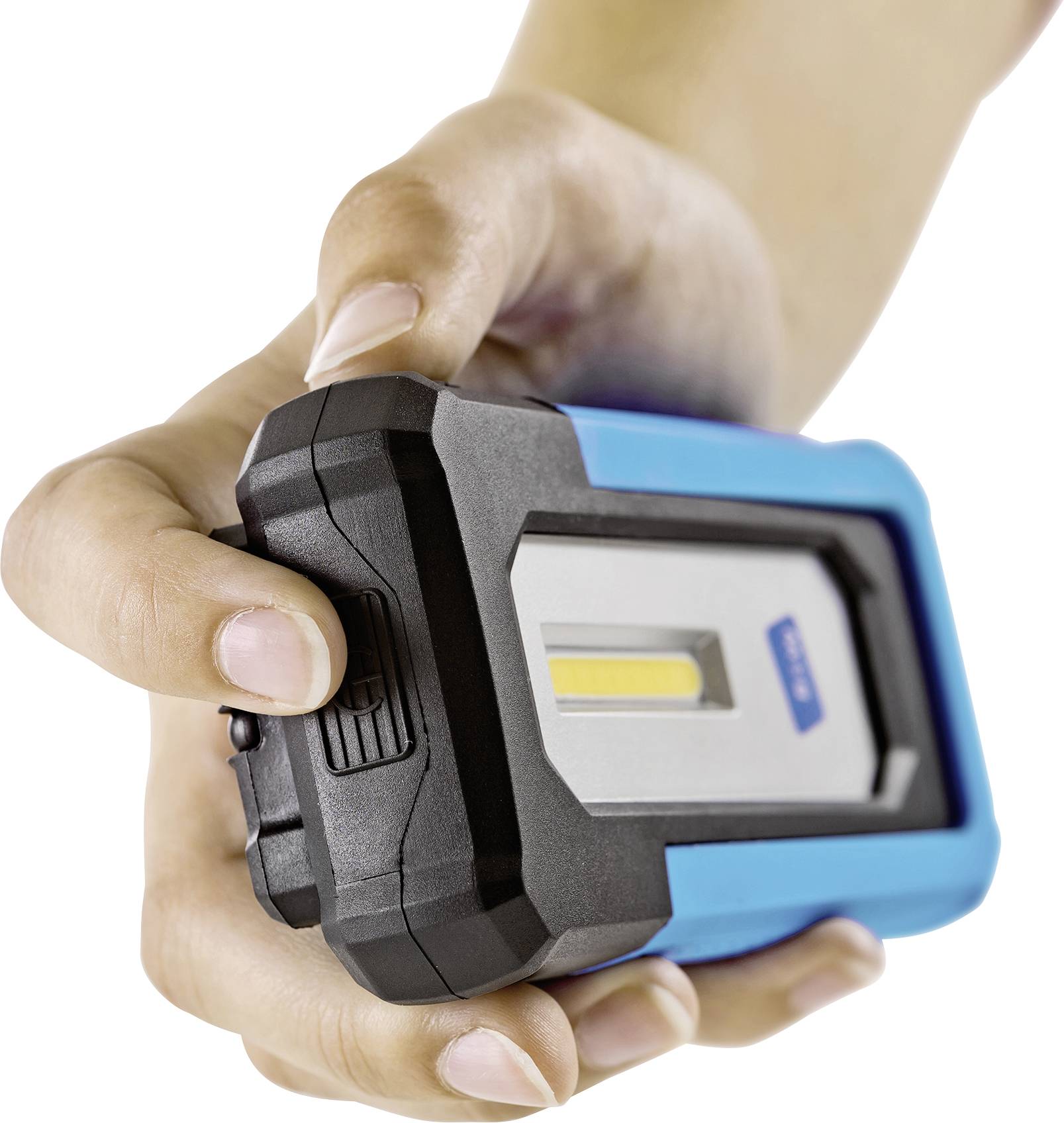 A hand is holding a portable blue and black work light with a yellow LED light against a silver background.