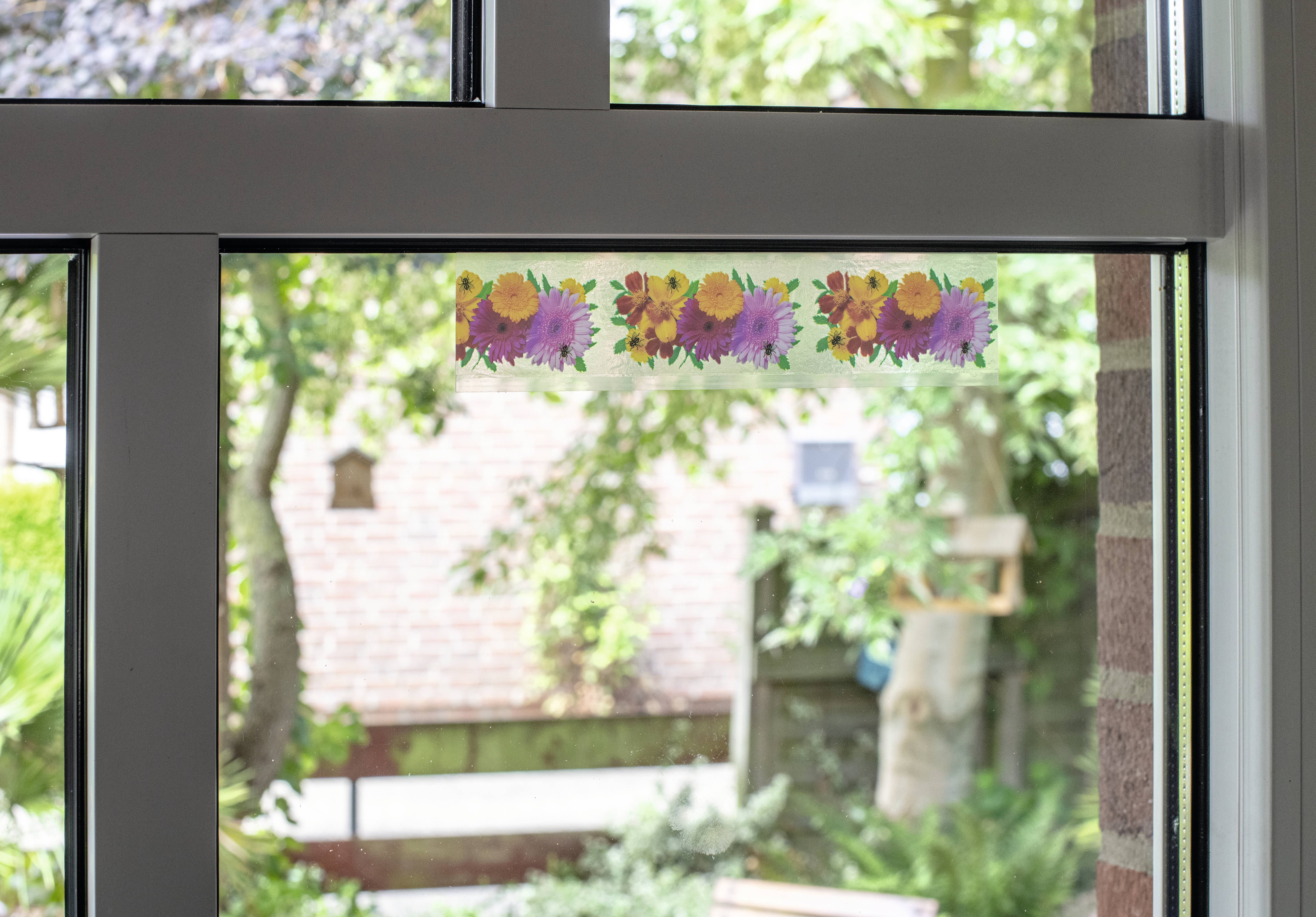 Floral decoration above a window overlooking a green garden.