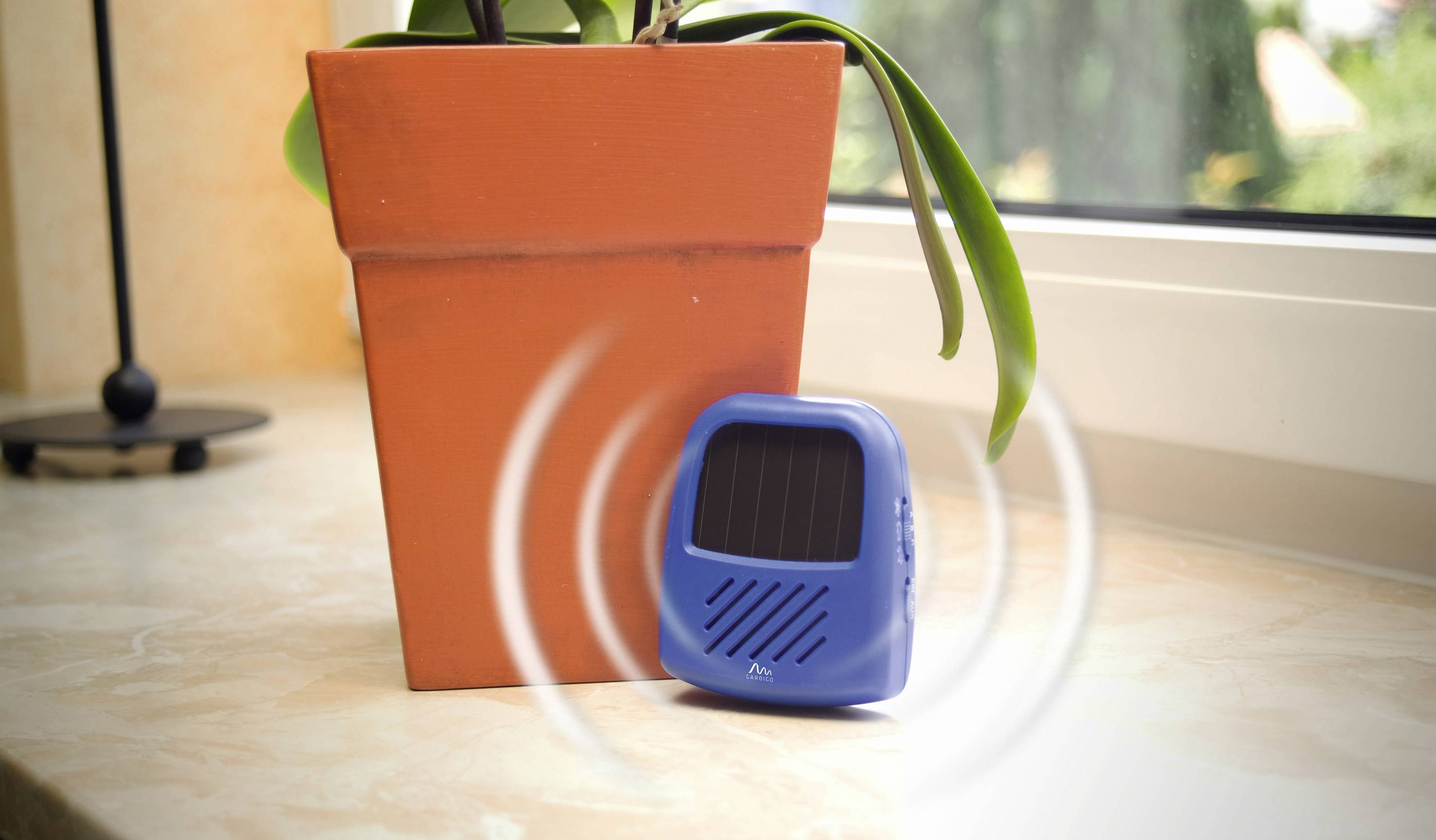 A blue electronic marten deterrent stands next to an orange flowerpot on a windowsill.