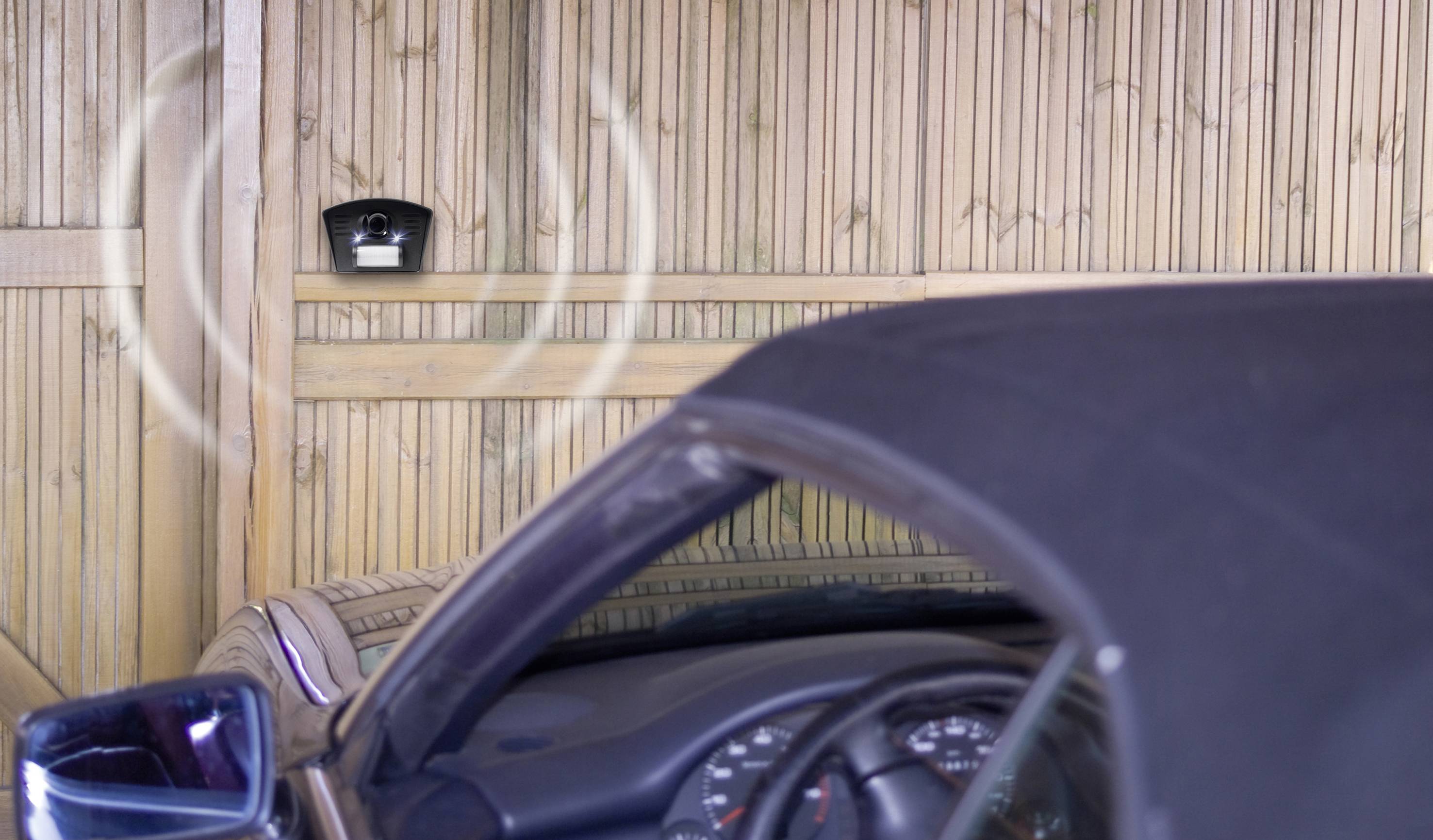 A car is parked in a garage. A sensor on the wall is blinking and helps with parking by indicating the distance to the wall.