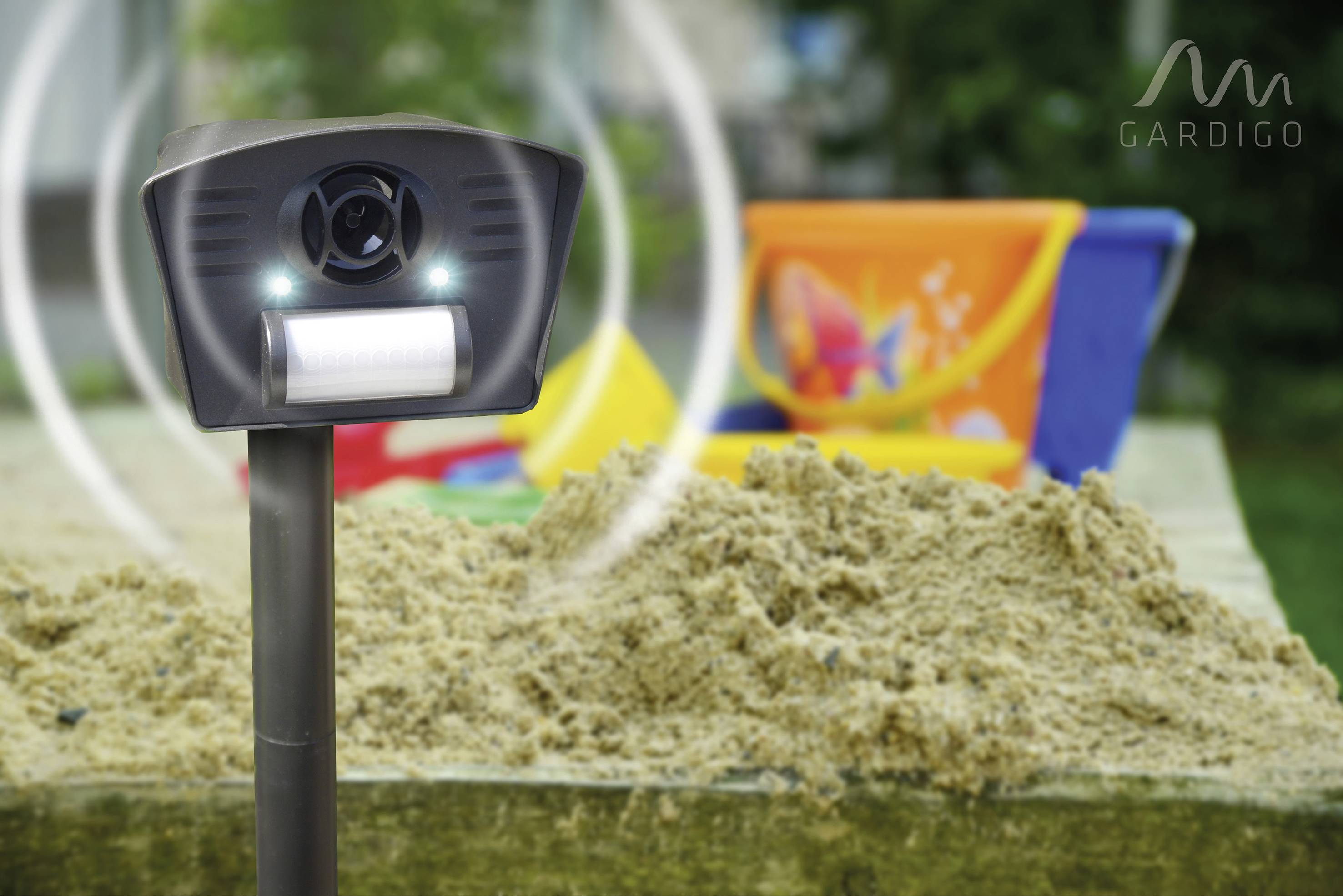 'Ultrasonic animal deterrent next to sandpit and colourful bucket in the garden. Suitable for deterring animals such as cats and dogs.'