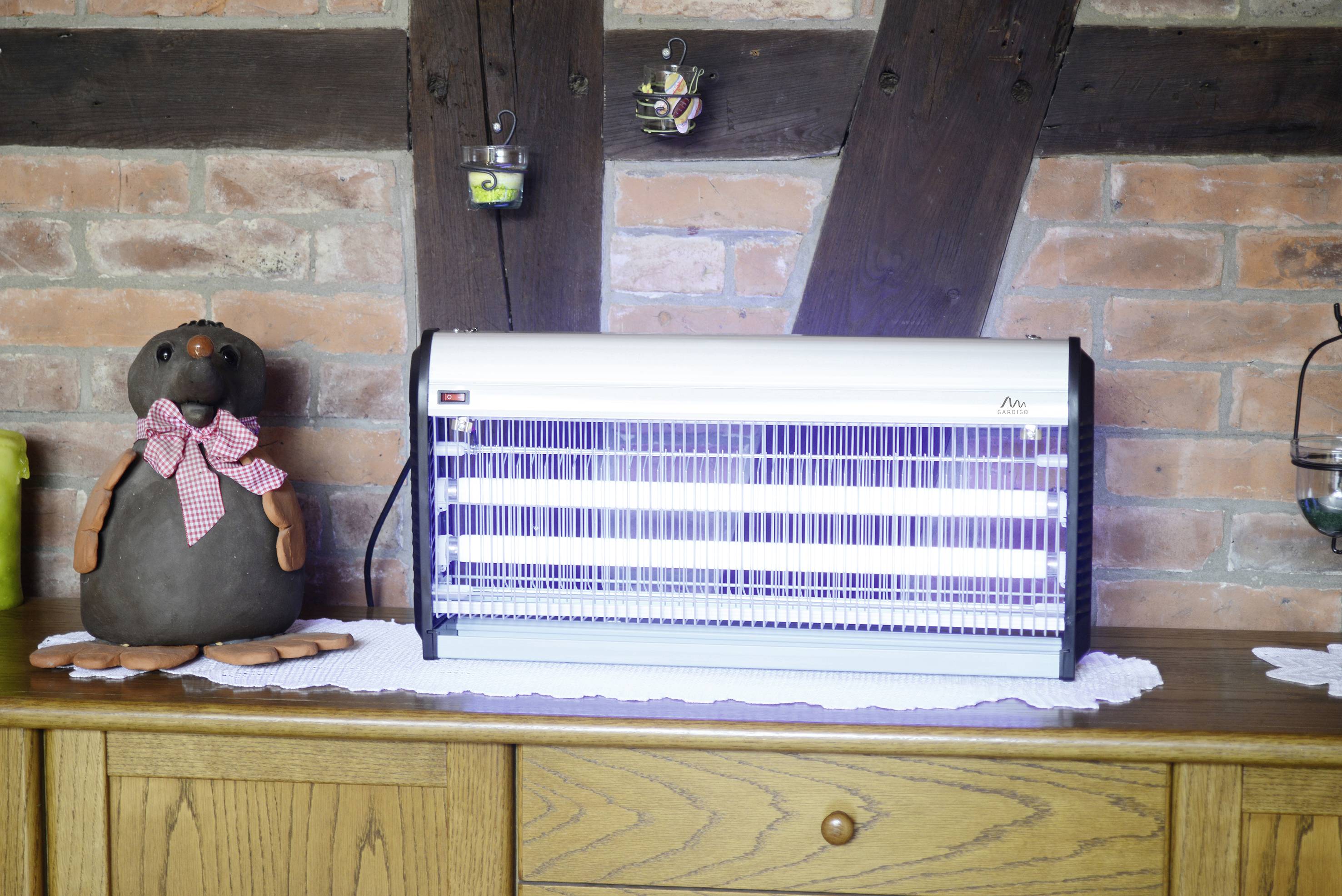 An insect killer with UV light sits on a wooden table in front of a brick wall. Next to it sits a fabric figure of a rat.