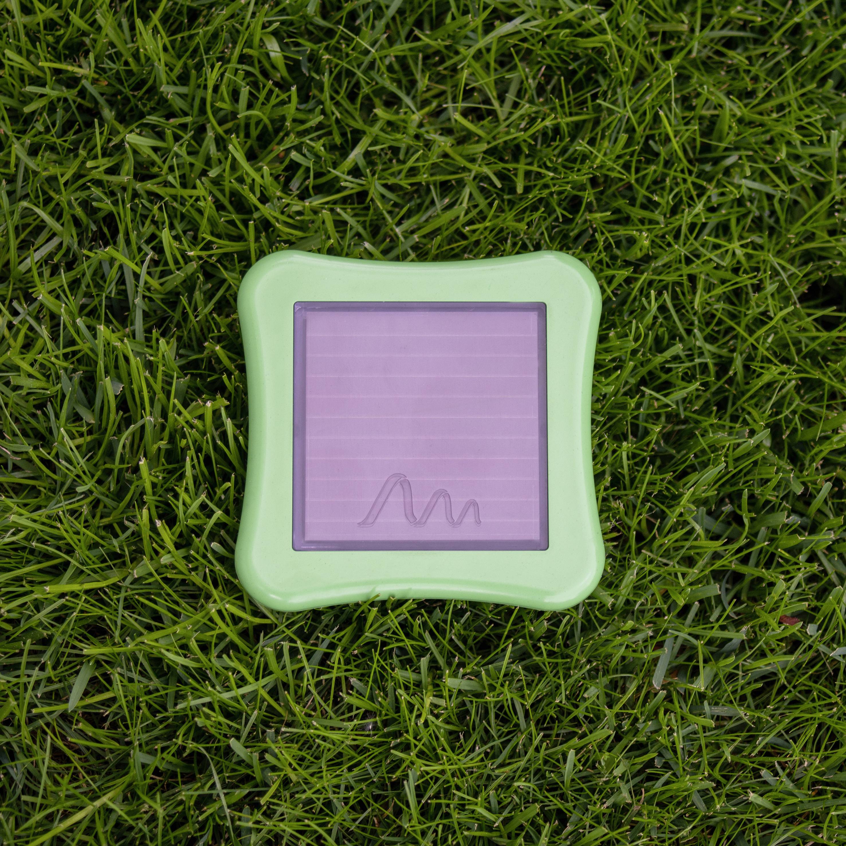 Green plastic frame with a solar panel in the centre, lying on grass.
