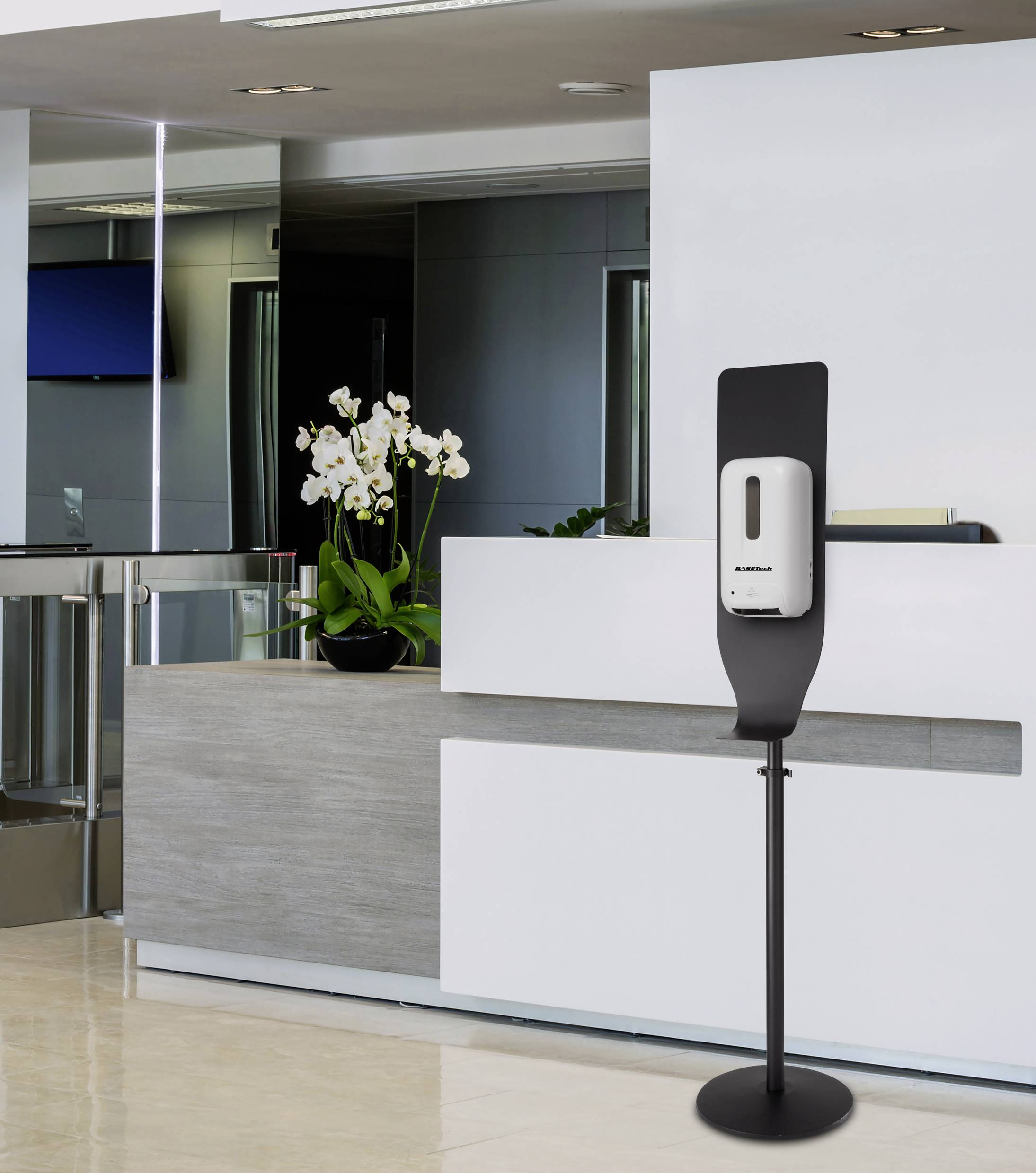 Hand sanitiser dispenser on a stand in front of a reception desk with a white orchid. Modern, bright lobby.