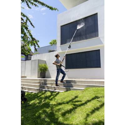 A person is cleaning the window shutters of a modern white house with a long pressure washer. Sunny day, green lawn.