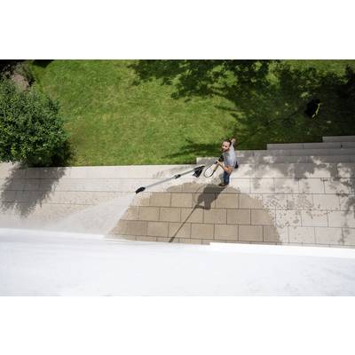 A man is cleaning stone steps of an outdoor staircase with a pressure washer. Green grass can be seen in the background.