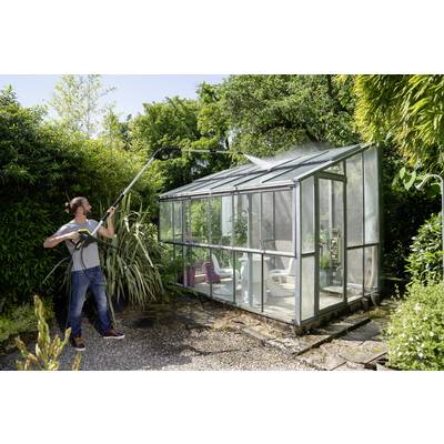 A person is cleaning a greenhouse with a pressure washer. It is sunny, and the greenhouse is situated in a green garden.