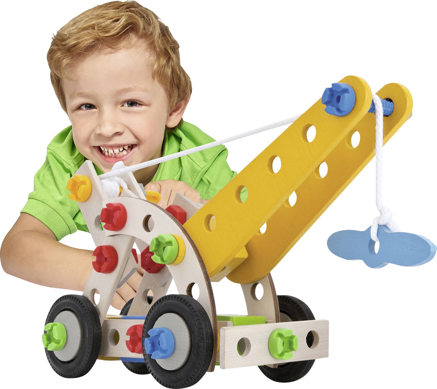 A child in a green shirt is playing with a colourful wooden crane with wheels, rope, and hook, smiling happily.