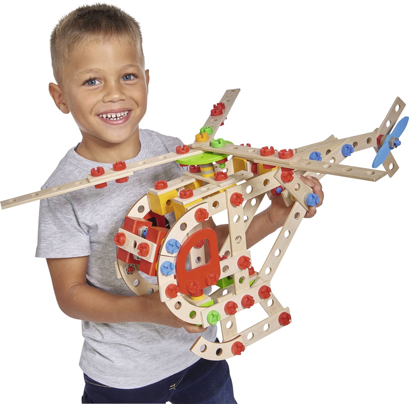 A child is holding a homemade helicopter model made from colourful building blocks, smiling happily.